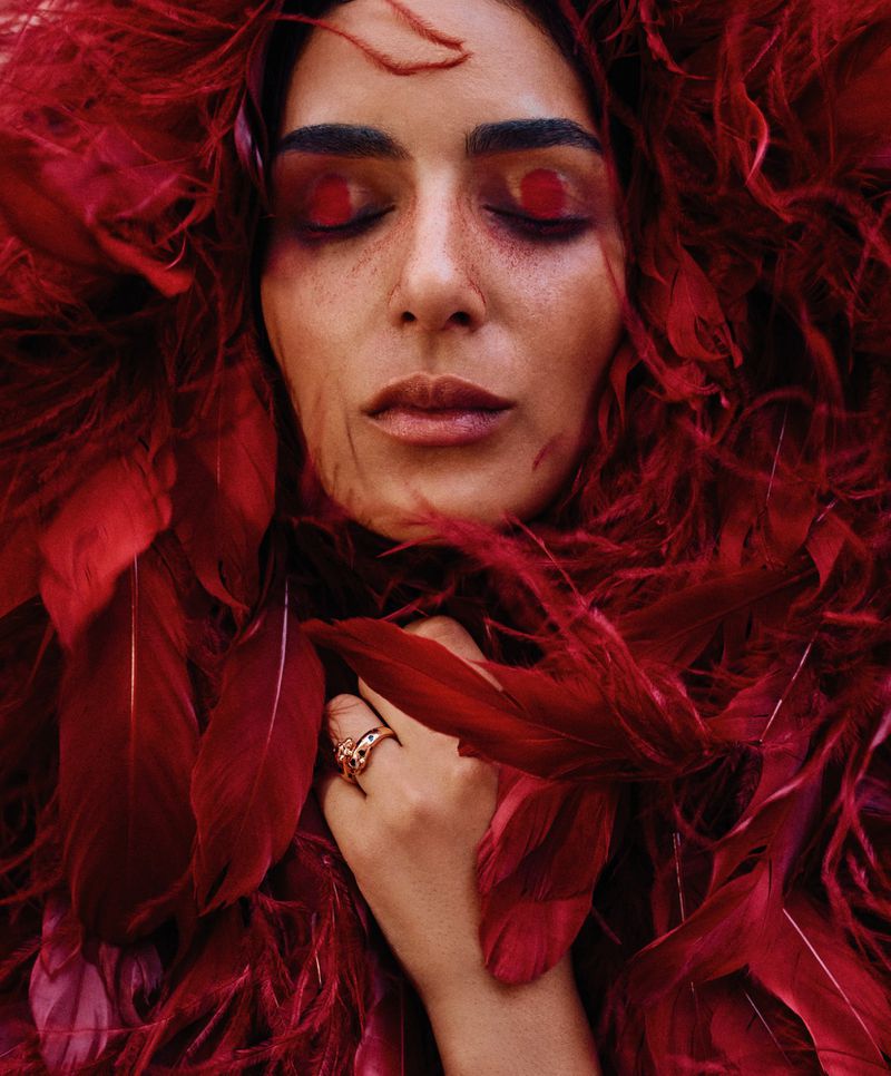 Model Nora Attal framed by dramatic red feathers with artistic eye makeup for T: The New York Times Style Magazine MENA