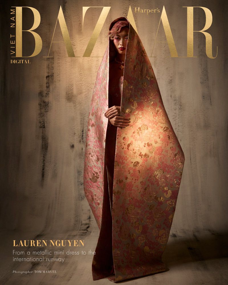 Model Lauren Nguyen wrapped in a large patterned pink and gold fabric standing against a textured backdrop for Harper's Bazaar Vietnam.
