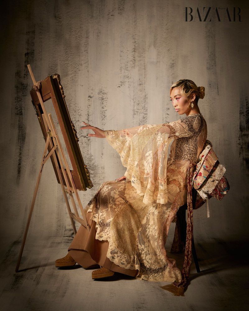 Model Lauren Nguyen in patterned gown seated beside an artist easel for Harper's Bazaar Vietnam