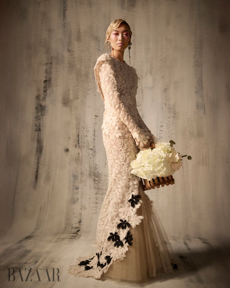 Model Lauren Nguyen in a textured cream gown holding a floral basket against a distressed neutral wall