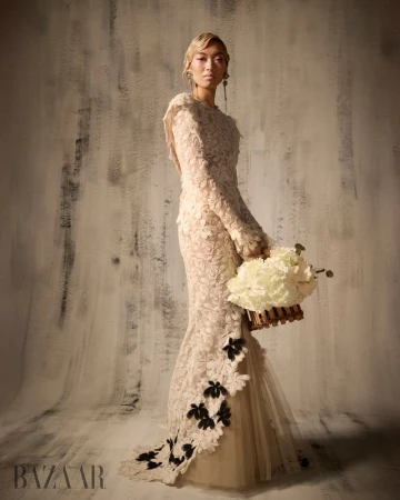 Model Lauren Nguyen in a textured cream gown holding a floral basket against a distressed neutral wall