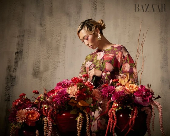 Model Lauren Nguyen arranging vibrant floral arrangements in a Harper's Bazaar Vietnam editorial shoot against a textured concrete wall.