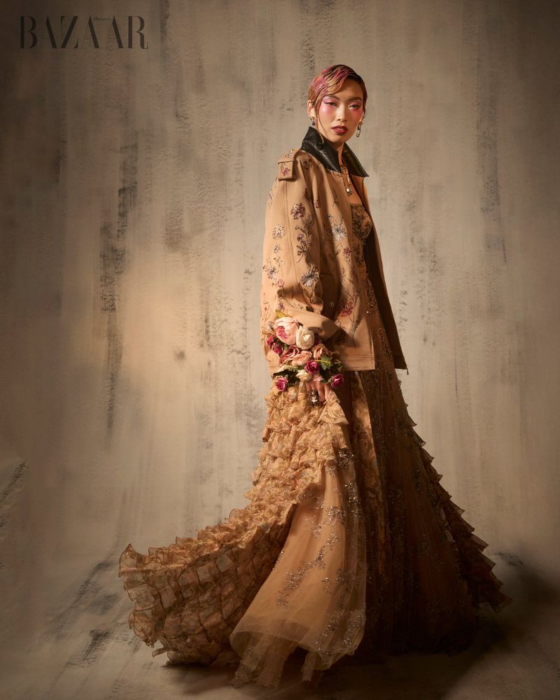 Model Lauren Nguyen in a tan embroidered jacket and tiered tulle gown against a textured studio background for Harper's Bazaar Vietnam.