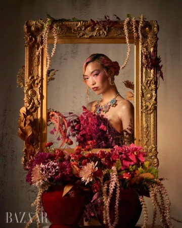 Model Lauren Nguyen posed behind an ornate gold picture frame adorned with floral arrangements and draped hanging plants.