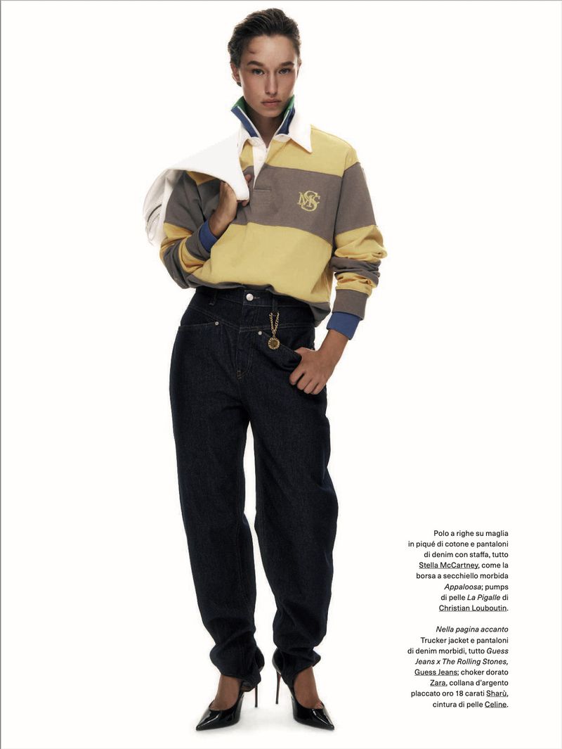 Model wearing a striped rugby shirt and dark jeans holding a white jacket against a white background