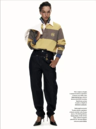 Model wearing a striped rugby shirt and dark jeans holding a white jacket against a white background