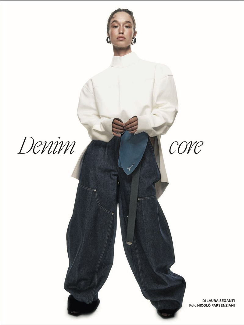 Model Jenn du Puy wearing wide-leg dark denim jeans and a white high-neck top against a plain white studio backdrop.