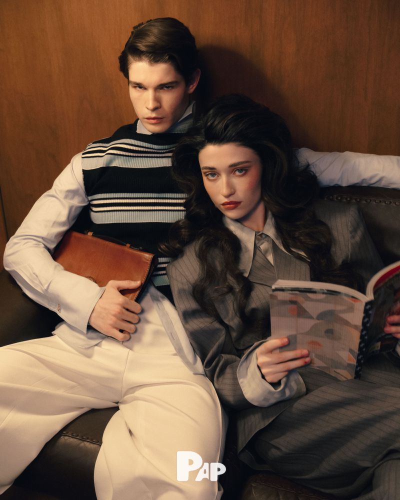Two models seated together on a leather sofa, a man holding a briefcase and a woman reading a magazine for PAP Magazine Saints of 79 editorial