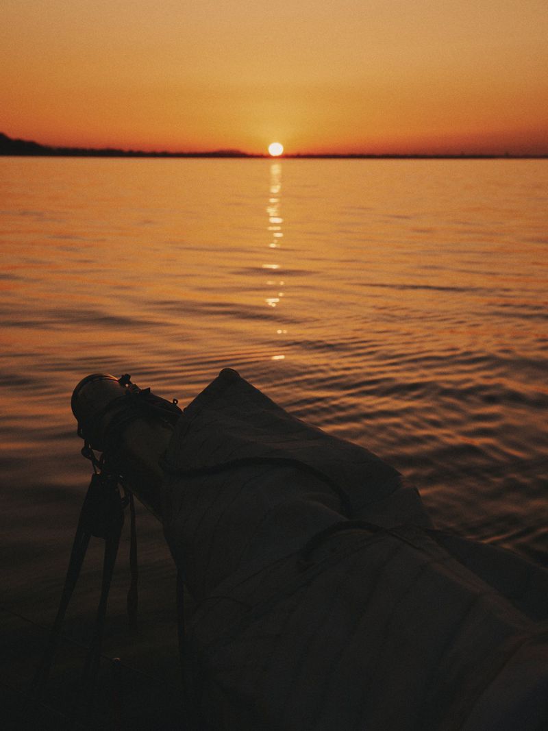 Scenic shot of a telescope pointed at the sunset on the ocean horizon, golden hour lighting casting a warm glow over the tranquil water.