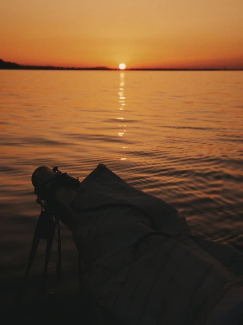 Scenic shot of a telescope pointed at the sunset on the ocean horizon, golden hour lighting casting a warm glow over the tranquil water.