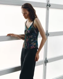 Model Kate McNamara wearing a dark patterned tank top and black trousers against a large white frosted window.