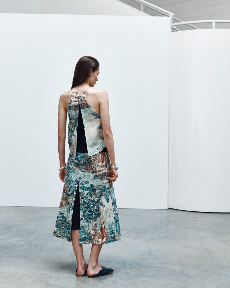 Model seen from behind wearing a patterned halter top and matching skirt in a modern white studio interior.