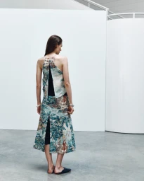Model seen from behind wearing a patterned halter top and matching skirt in a modern white studio interior.