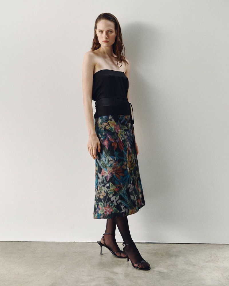 Model wearing a black top and a patterned floral skirt against a plain wall for ACCORDA SS27