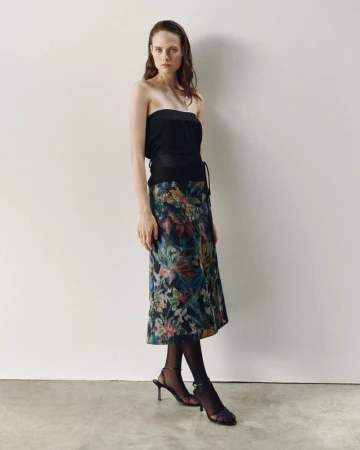 Model wearing a black top and a patterned floral skirt against a plain wall for ACCORDA SS27