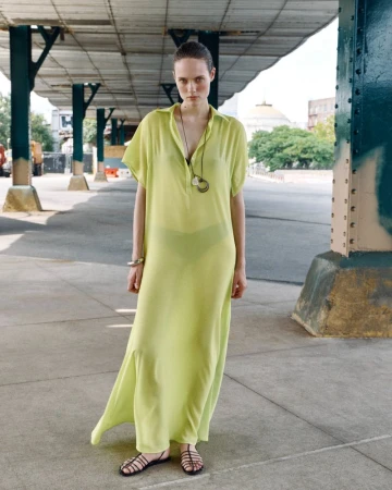 Model wearing a sheer yellow lime dress standing beneath a bridge structure for ACCORDA SS27 lookbook