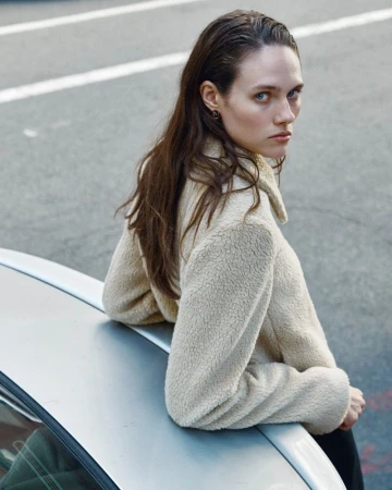 Model in cream textured jacket leaning against a silver car on asphalt road