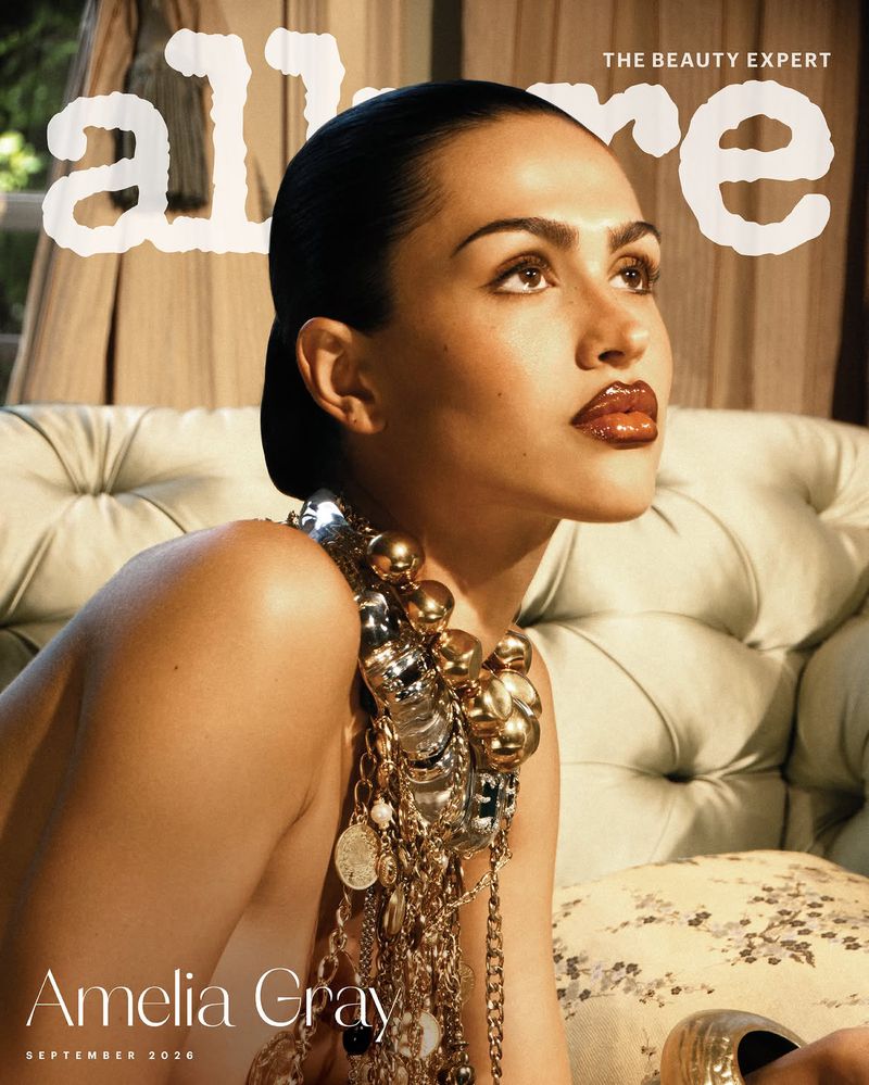 Model Amelia Gray seated against a tufted sofa wearing statement metallic jewellery for Allure Magazine September 2026