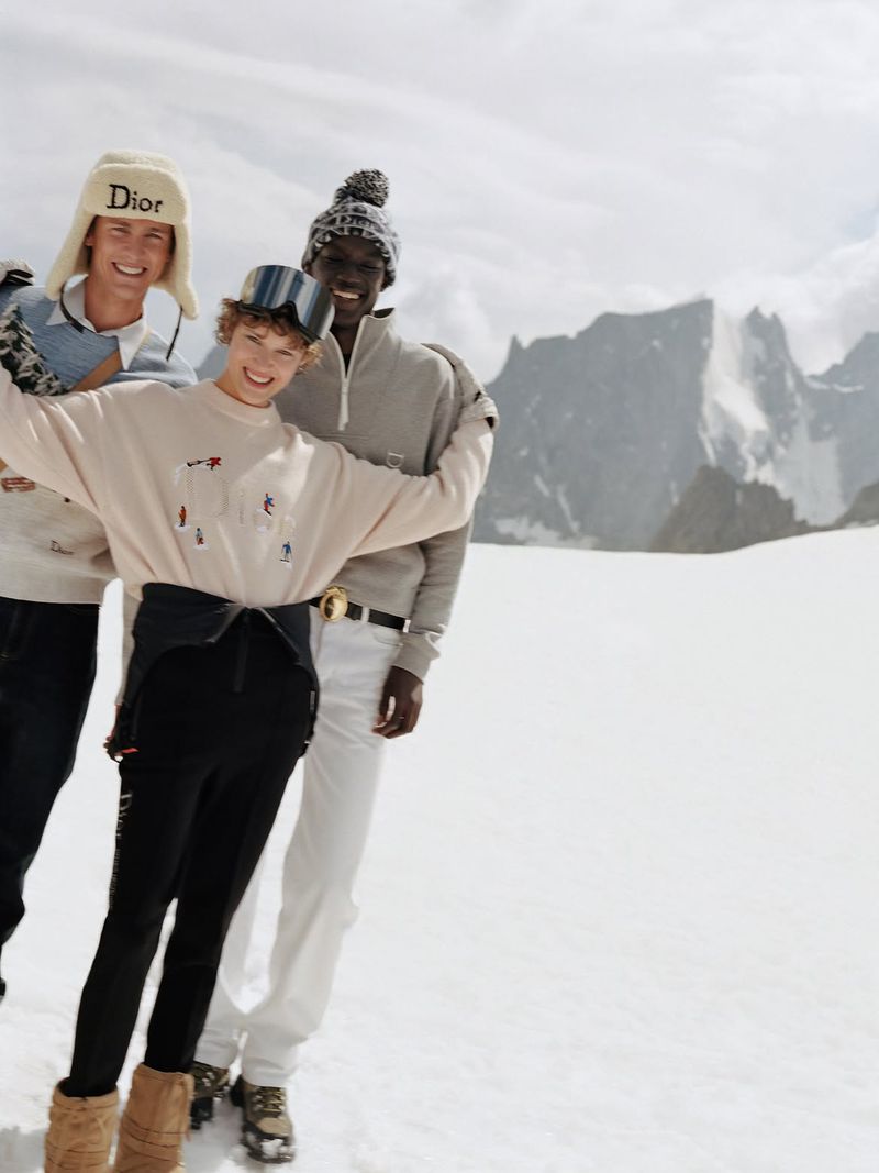 Three models in winter apparel posing together outdoors on a snowy mountain range for the Dior Alps campaign.