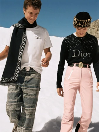 Two models outdoors on snowfield, man wearing white t-shirt and patterned trousers, woman wearing black sweater and pink ski pants