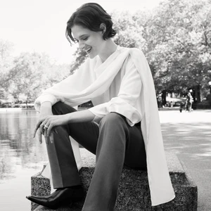 Monochrome portrait of Louisa Jacobson seated outdoors wearing a white draped blouse and dark trousers for American Vogue, photographed by Tess Ayano.