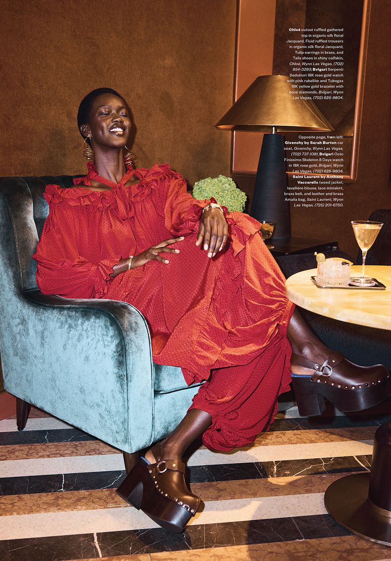 Model wearing a red ruffled dress and platform clogs seated in a blue velvet armchair for Modern Luxury editorial