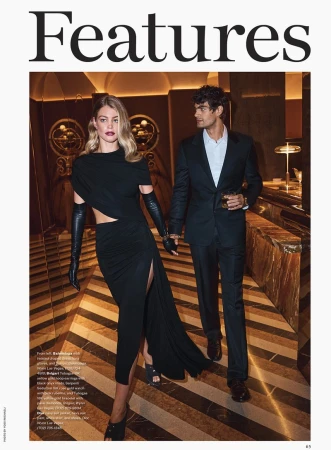 Two models walking through a hotel lobby, wearing black eveningwear and holding hands.