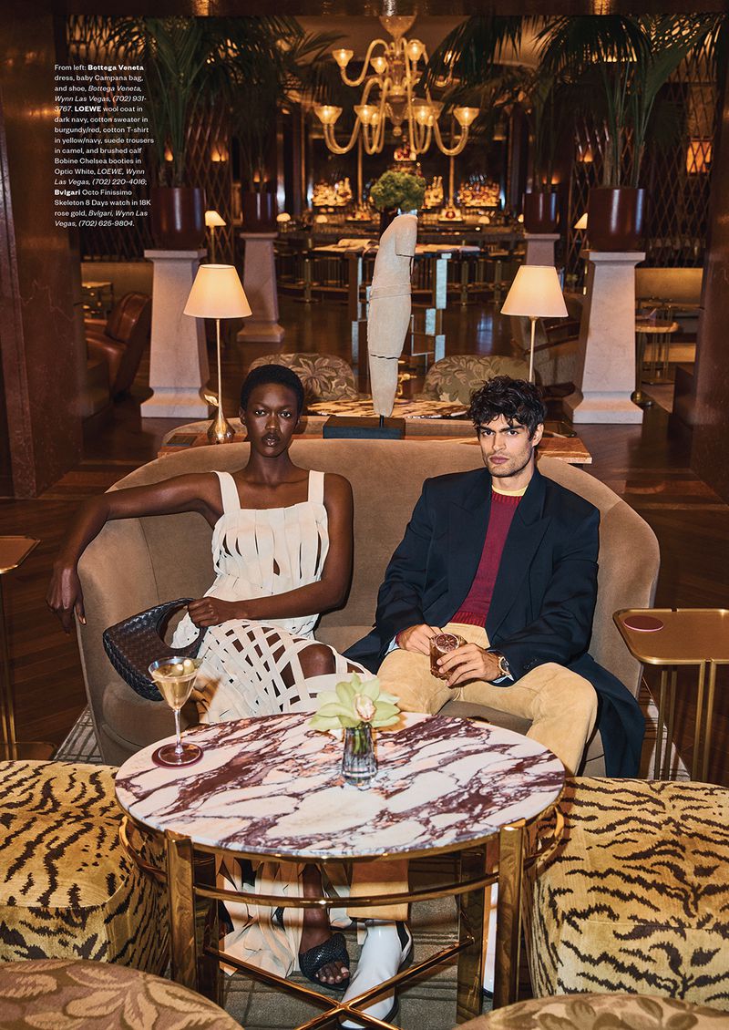 A man and a woman seated on a curved sofa in a luxurious lounge setting with a round marble table in the foreground.