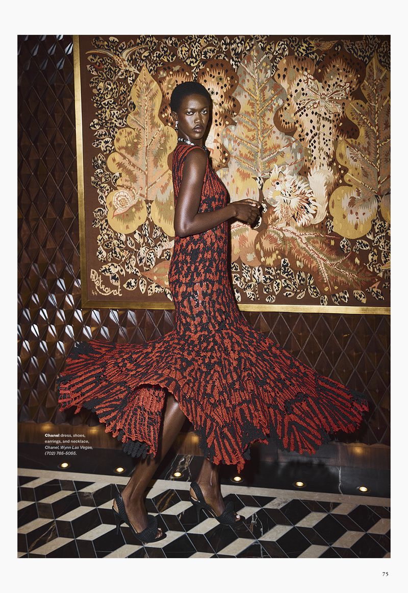Model wearing a patterned red and black dress standing in front of an ornate tapestry and tiled floor.