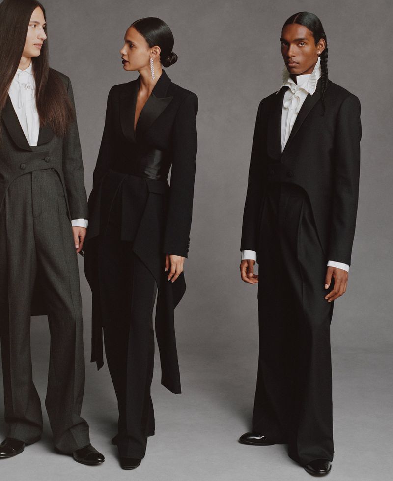Three models wearing formal black tuxedos and white ruffled shirts against a neutral grey studio background.