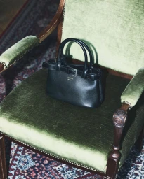 Black leather handbag resting on a vintage green velvet armchair with dark wooden trim