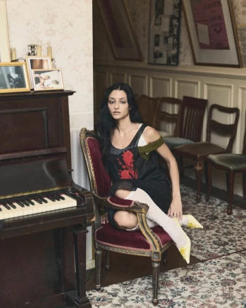 Sofie Royer seated on a vintage armchair next to an upright piano in Numéro Berlin editorial by Emil Dietrich