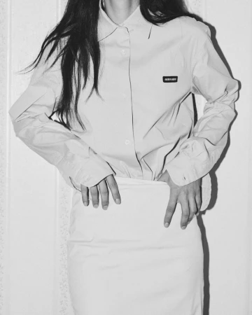 Monochrome portrait of a woman with dark hair wearing a button-down shirt and skirt, hands resting on hips.