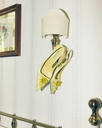 A pair of yellow designer slingback heels hung over a wall lamp against floral wallpaper for Numéro Berlin by Emil Dietrich.