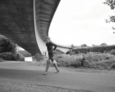 Model walking on a path beneath a large concrete bridge structure for L'Obs Magazine editorial by Giuseppe Triscari.