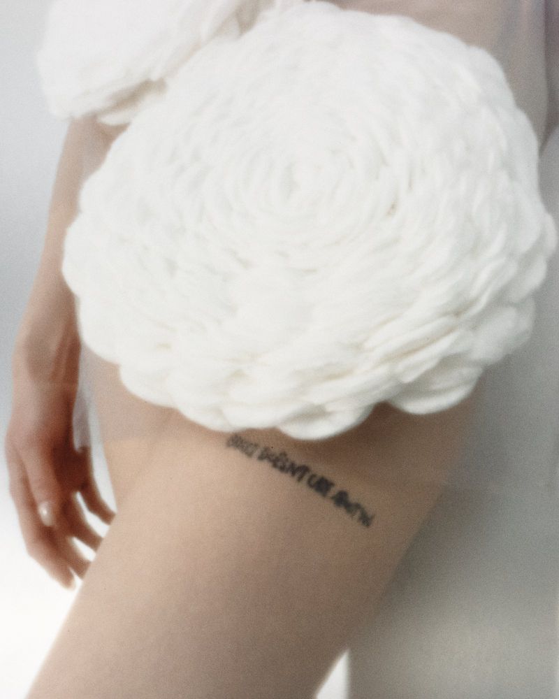 Close-up portrait of a model wearing a white ruffled textile garment with text tattoo on leg for Tidal Magazine