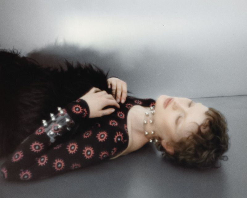 Model lying on a grey studio floor wearing a patterned black top and silver studded jewellery for Tidal Magazine editorial