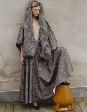 Model Camille Chifflot wearing a patterned grey dress and fur hood, posing with a ceramic urn for 10 Magazine USA