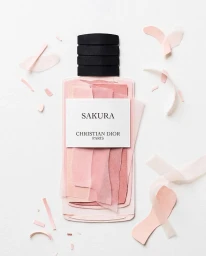 A stylized paper art Dior Sakura perfume bottle surrounded by pink paper cutouts on white background.