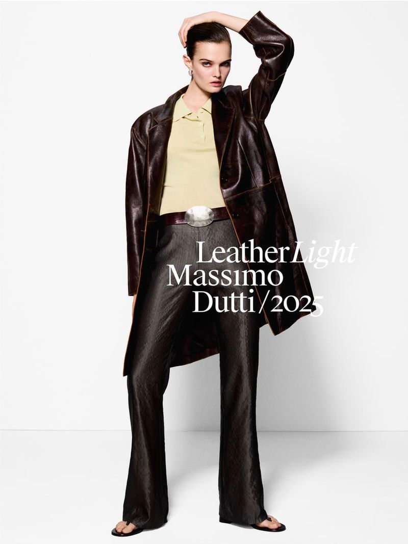 Fashion editorial shot: a female model poses in a brown leather coat and wide-leg pants against a white backdrop in a studio setting.