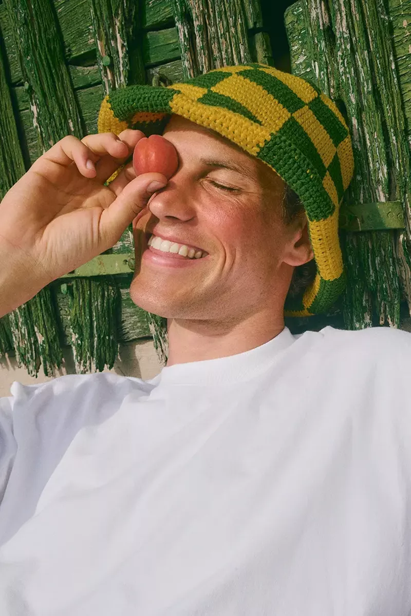 Model Paul Hupfer holding a peach over his eye while wearing a green and yellow checkered crochet bucket hat.