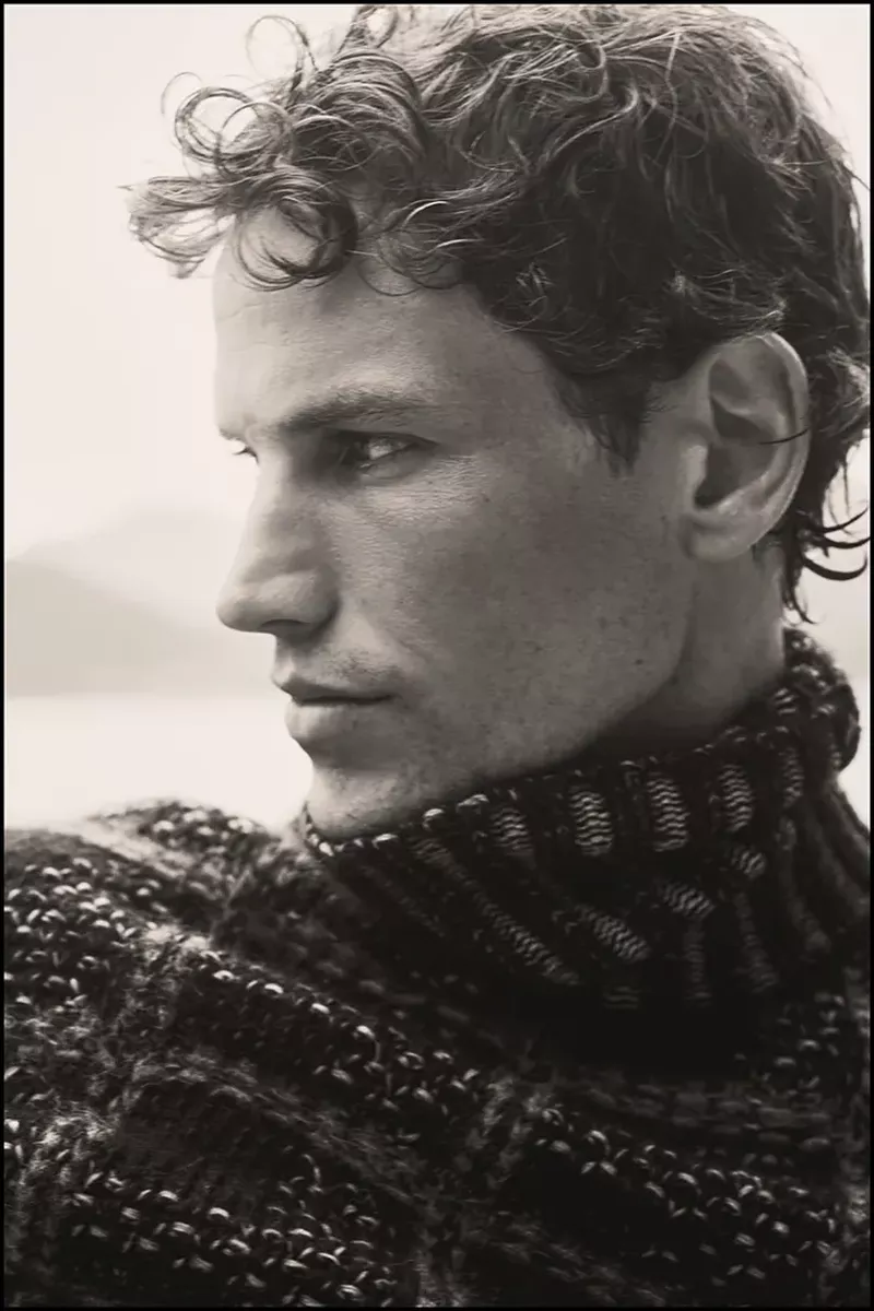 Portrait of model Paul Hupfer wearing a textured dark turtleneck sweater in profile view against an overcast background