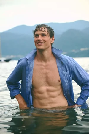 Model Paul Hupfer standing in water wearing an unbuttoned blue shirt, photographed by Oksana Baranchykova for MMScene.