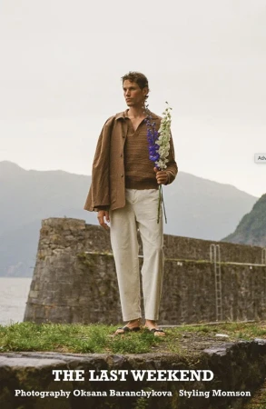 Model Paul Hupfer holding flowers outdoors near a stone wall with mountains in the background for MMScene editorial
