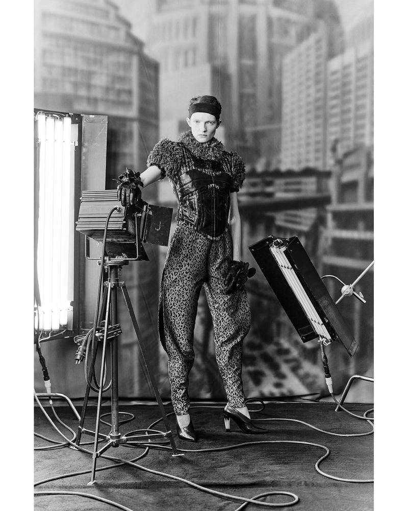 Model Sophia Friesen in patterned apparel posing among studio lights against a painted cityscape backdrop