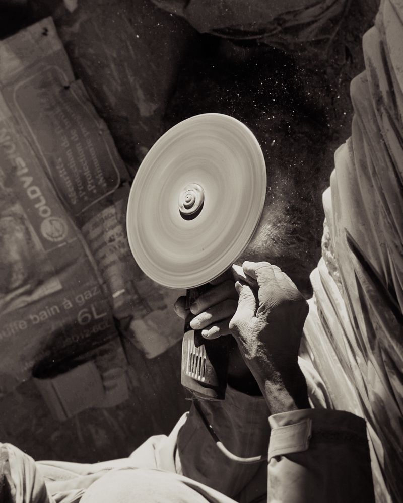 Close-up shot of a person using a circular power tool, kicking up fine dust particles in a workshop environment.