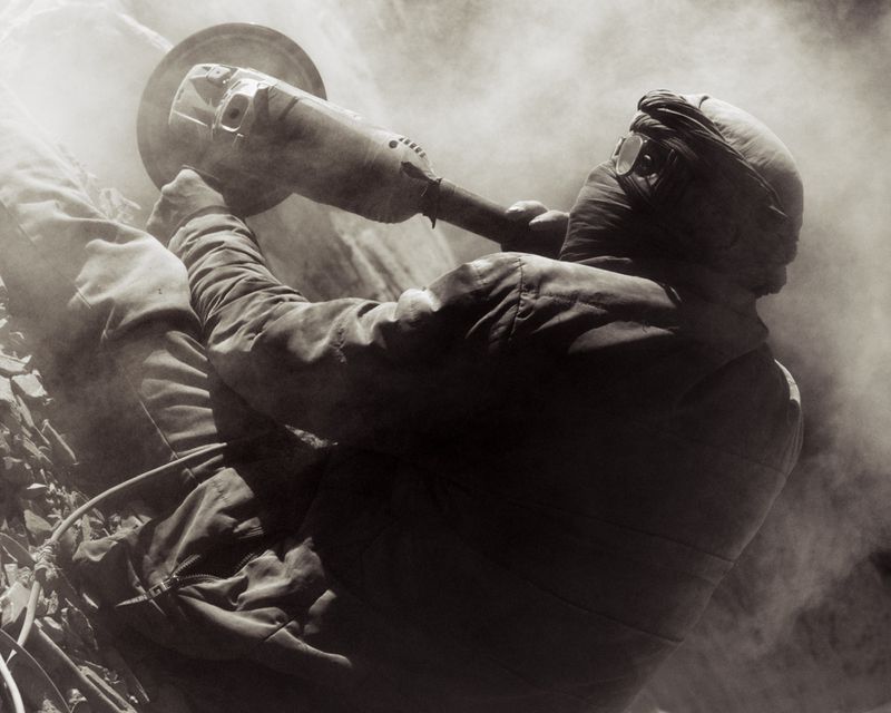 Worker in protective gear and goggles using an angle grinder amid heavy dust and smoke for Atmos Magazine