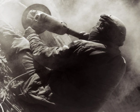 Worker in protective gear and goggles using an angle grinder amid heavy dust and smoke for Atmos Magazine
