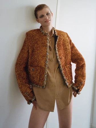 Model wearing a textured orange tweed jacket and tan shirt leaning against a plain white wall
