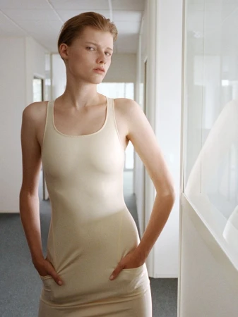 Model in cream tank dress standing in an office hallway for AnOther Magazine